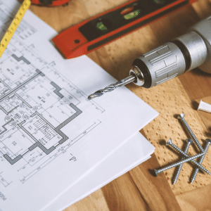 A drill on a table with plans for home improvement projects