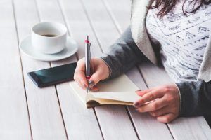 woman writing in notebook with coffee and phone
