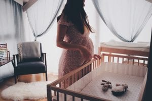 a pregnant woman standing in front of a crib