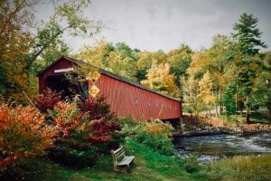a covered bridge in the fall with trees and a bench
