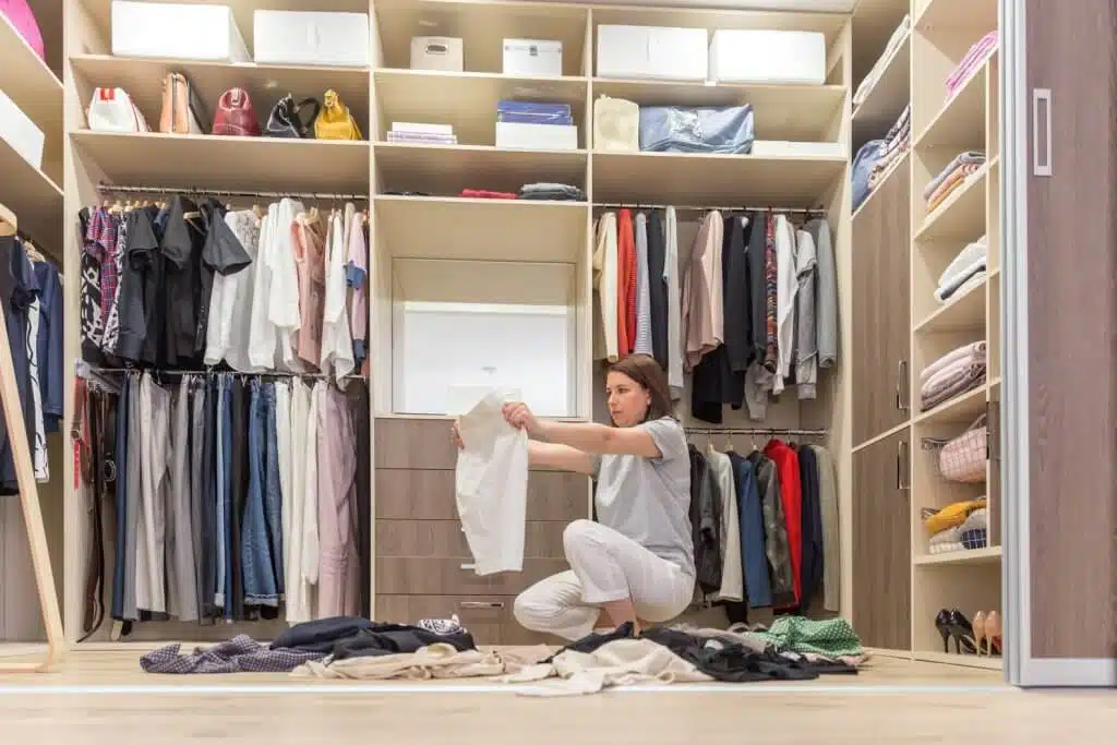 woman sitting on the floor in a closet sorting clothes to declutter
