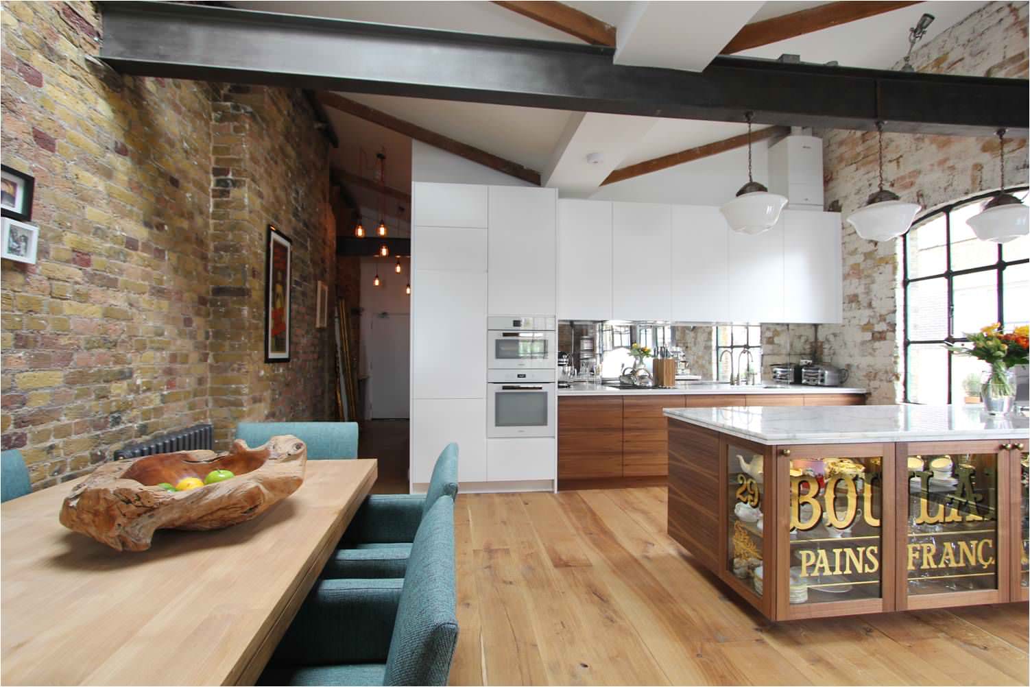 Modern kitchen and dining area featuring reclaimed brick walls, exposed steel beams, salvaged wood flooring, and contemporary cabinetry that blend historic building materials with modern design.