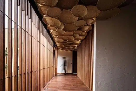 Hallway featuring reclaimed wood wall slats, warm wood flooring, and a ceiling installation made from repurposed woven baskets, demonstrating creative use of reclaimed materials in contemporary interior design.