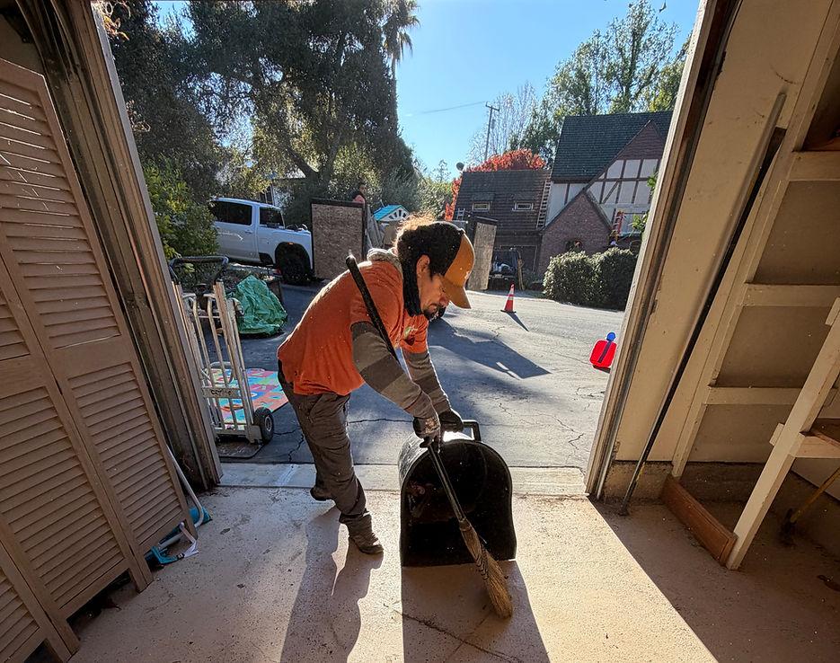 Worker sweeping renovation debris into a dustpan during a residential home cleanup.