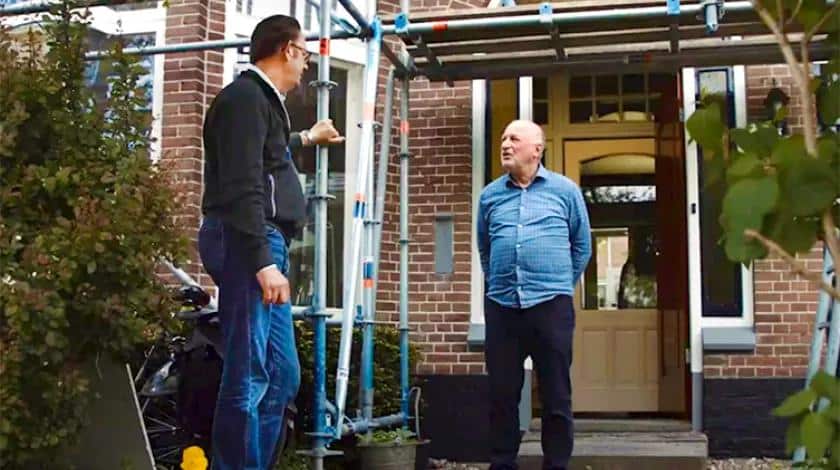 Two men talking outside a brick home surrounded by scaffolding during a renovation project.