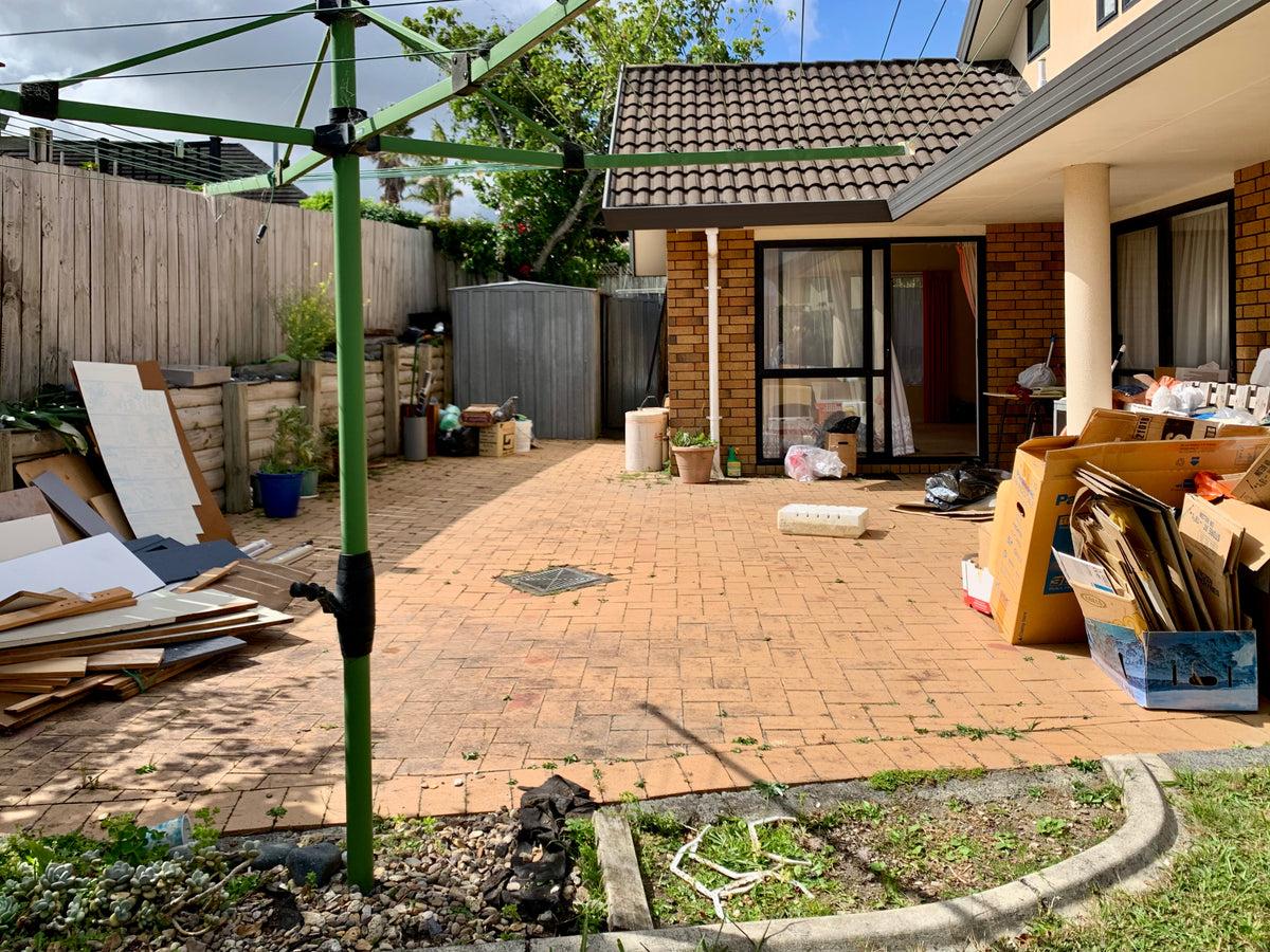 Cluttered backyard patio with cardboard, wood scraps, and debris before an outdoor renovation.